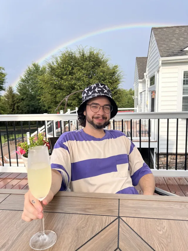 Bryan on a patio raising a glass with a rainbow arcing overhead